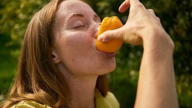 Ein Frau isst eine Orange in einem Orangenhain. Das Immunsystem ist ein Schutzschild, das den Körper vor Krankheitserregern schützt. Ausreichend Schlaf und eine vitaminreiche Ernährung helfen die Körperabwehr zu stärken.  | Bild: picture alliance / Westend61 | Anastasiia Nelen