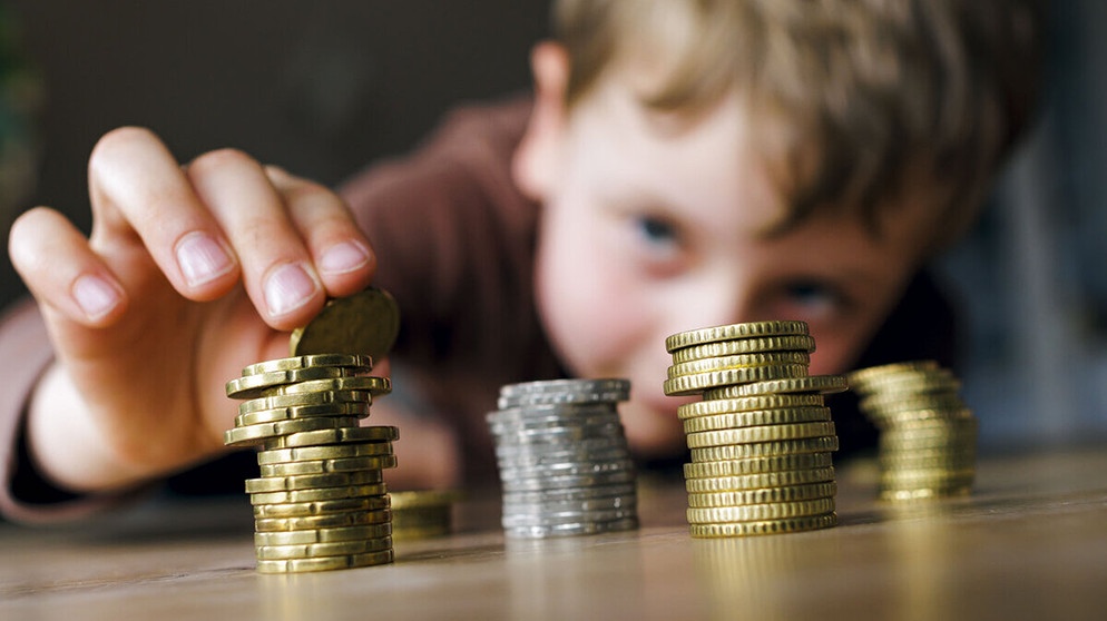 Ein kleiner Junge stapelt seine Münzen. Finanzbildung in der Schule? Schön wär's. Tatsächlich lernen Kinder den Umgang mit Geld häufig von den Eltern. Wie ihr eurem Kind beim Sparen und Anlegen helft, und welche Rolle Taschengeld dabei spielt. | Bild: picture alliance / photothek | Thomas Trutschel