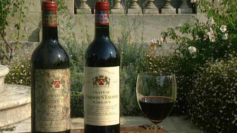 Zwei Weinflaschen und ein Glas Rotwein stehen auf einem Tisch. | Bild: BR