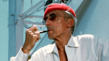 Taucher Jacques-Yves Cousteau mit seinem Markenzeichen, einer roten Mütze - Cousteau tauchte in Tiefen ab, die vor ihm noch niemand erforscht hatte. Mit Dokumentarfilmen brachte er die Tiefsee erstmals in die Wohnzimmer der Zuschauer. | Bild: picture alliance / ASSOCIATED PRESS | The Cousteau Society