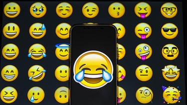 Ein Tränen-lach-Smiley vor einem Hintergrund aus anderen Emojis. Der Smiley ist aus unserer digitalen Kommunikation nicht wegzudenken, ob als Grafik oder als Tastenkürzel :-) Was Emojis bedeuten und wie sie die Sprache verändern. | Bild: picture alliance / AA | Aytavß vúnal