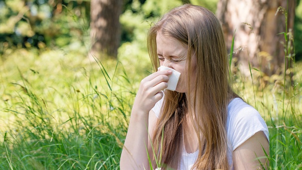 Symbolbild Heuschnupden / Pollenallergie: Junge Frau mit langen blonden Haaren sitzt auf einer Wiese und schnäuzt in ein Taschentuch. | Bild: colourbox.com