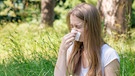 Symbolbild Heuschnupden / Pollenallergie: Junge Frau mit langen blonden Haaren sitzt auf einer Wiese und schnäuzt in ein Taschentuch. | Bild: colourbox.com