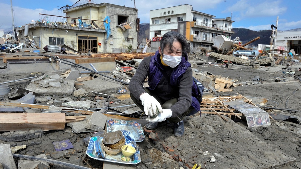 Eine Frau sucht in den Trümmern nach Geschirr ihres Restaurants, das im Tsunami weggerissen wurde, in Ofunato in der Präfektur Iwate im Nordosten Japans nach dem schweren Erdbeben vom 11. März 2011. Eine weitere Folge der Naturgewalt war die Nuklearkatastrophe von Fukushima. | Bild: picture alliance  dpa  Kimimasa Mayama