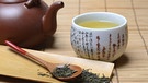 Eine Tasse japanischer Grüner Tee und Teeblätter. Tee bezeichnet nicht nur das Getränk, sondern eine uralte Kulturpflanze, die sich im Lauf der Geschichte durch Handel und Globalisierung auf der ganzen Welt verbreitet hat. | Bild: picture alliance / imageBROKER/Jürgen Pfeiffer 
