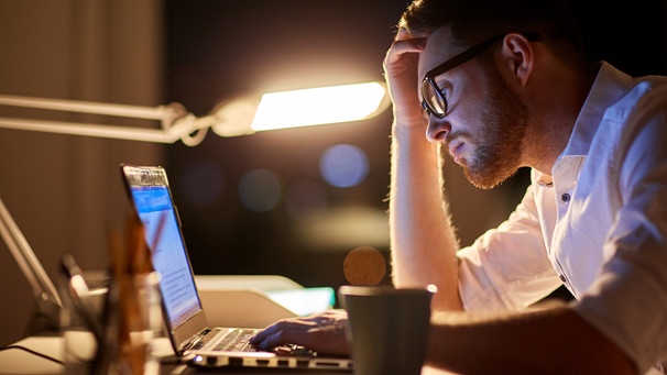 Ein Mann arbeitet bis spät in die Nacht an seinem Laptop, sieht unglücklich aus. Ob beim Sport, in der Beziehung oder im Beruf, Durchhaltevermögen ist überall gefragt. Doch ab wann wird durchhalten schädlich? Darauf könnt ihr achten. | Bild: colourbox.com/ Syda Productions