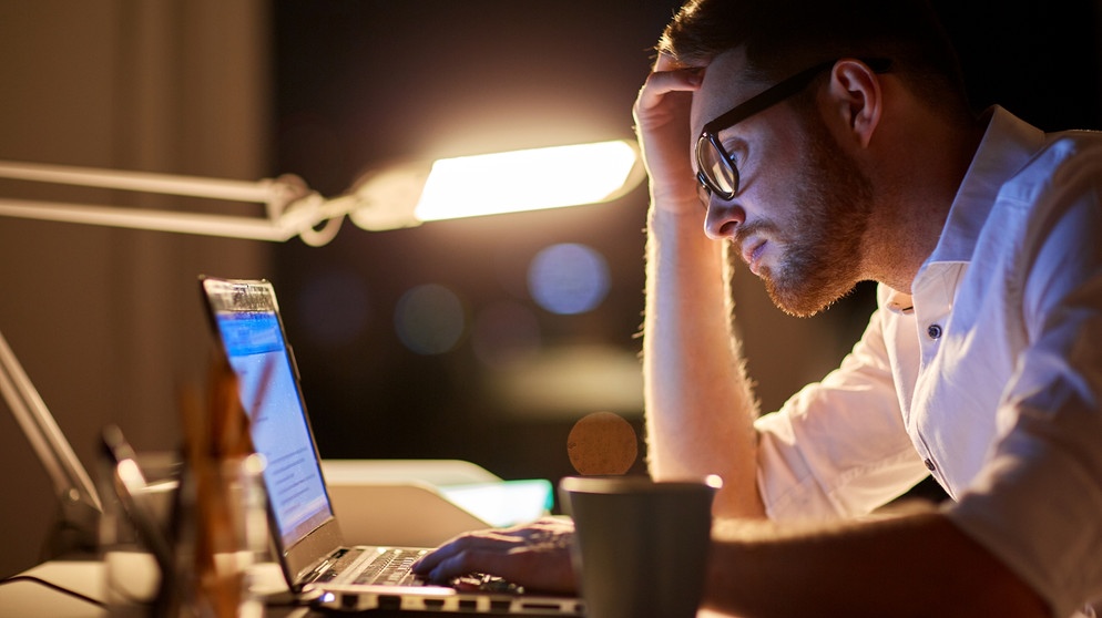 Ein Mann arbeitet bis spät in die Nacht an seinem Laptop, sieht unglücklich aus. Ob beim Sport, in der Beziehung oder im Beruf, Durchhaltevermögen ist überall gefragt. Doch ab wann wird durchhalten schädlich? Darauf könnt ihr achten. | Bild: colourbox.com/ Syda Productions