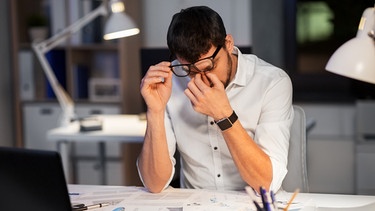 Ein Mann sitzt am Schreibtisch und reibt sich die Augen. Ob beim Sport, in der Beziehung oder im Beruf, Durchhaltevermögen ist überall gefragt. Doch ab wann wird durchhalten schädlich? Darauf solltet ihr achten. | Bild: colourbox.com