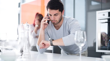 Ein Mann telefoniert und schaut dabei auf seine Armbanduhr. Viele Menschen treibt die Angst um, in ihrer Freizeit etwas zu verpassen. Wir haben Tipps gegen FOMO und Freizeitstress, damit ihr euch in eurer freien Zeit wirklich erholt. | Bild: picture alliance / Westend61 | zerocreatives