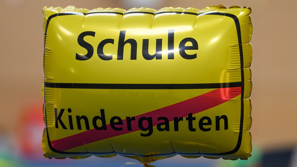 Ein gelber Heißluftballon ähnelt einem Ortsschild. Oben steht das Wort: Schule, unten steht durchgestrichen: Kindergarten. Was ist wichtig für einen erfolgreichen Schulanfang? Tipps, die eurem Kind den Start in der Grundschule erleichtern. | Bild: picture alliance/dpa/dpa-Zentralbild/Robert Michael