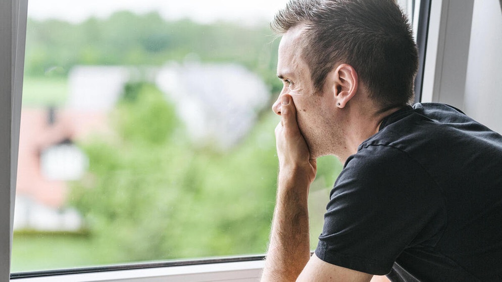 Ein Mann blickt nachdenklich aus dem Fenster. Angst kann uns schützen, aber auch lähmen. Welche Ursachen und Grundformen von Angst es gibt und Tipps, wie ihr Ängste überwindet. | Bild: picture alliance / CHROMORANGE | Michael Bihlmayer