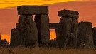 Der Sonnenaufgang färbt den Himmel über der UNESCO-Weltkulturerbestätte Stonehenge in orange-gelbes Licht.  | Bild: dpa-Bildfunk/Espa Photo Agency