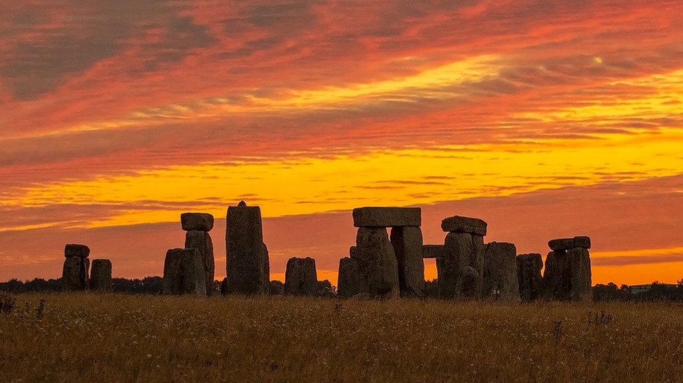 Der Sonnenaufgang färbt den Himmel über der UNESCO-Weltkulturerbestätte Stonehenge in orange-gelbes Licht.  | Bild: dpa-Bildfunk/Espa Photo Agency