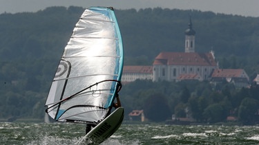 Surfer auf dem Ammersee. Der Wind beeinflusst er das Wetter, so viel ist klar. Er lässt die Sonne scheinen und treibt die Wolken an. Doch wie entstehen die Winde überhaupt? | Bild: picture-alliance/dpa