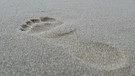 Fußabdruck im Sand an einem Strand | Bild: picture-alliance/dpa