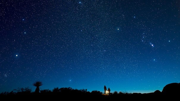 Zwei Menschen betrachten den Sternenhimmel. Am Himmel ist die Konstellation von Orion zu erkennen. Orion ist eine offiziell anerkannte Konstellation der Internationalen Astronomischen Union (IAU). Sternbilder helfen bei der Orientierung unter den Sternen. | Bild: picture alliance / All Canada Photos | David Nunuk