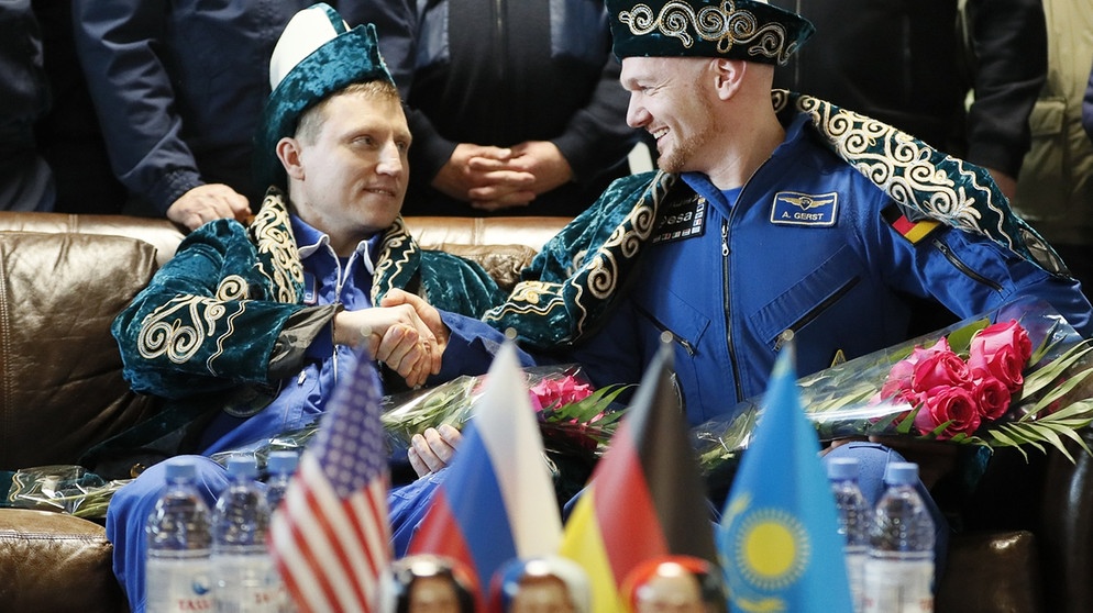 Kosmonaut Sergej Prokopjew (links) aus Russland und Astronaut Alexander Gerst aus Deutschland in kasachischer Tracht während einer Pressekonferenz am Flughafen in Scheskasgan, Kasachstan. Kurz zuvor waren die beiden zusammen mit ihrer US-amerikanischen Kollegin Serena Auñón-Chancellor an Bord einer Sojus-Raumkapsel auf der Erde gelandet, nachdem sie über ein halbes Jahr auf der Internationalen Raumstation ISS verbracht hatten. | Bild: dpa-Bildfunk/Shamil Zhumatov