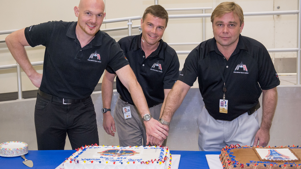 Am 19. März 2014 feiern die angehenden ISS-Bewohner Alexander Gerst (links), Reid Wiseman (Mitte) und Maxim Surajew (rechts) mit einer schicken ISS-Torte den Abschluss des Astronautentrainings in Houston. | Bild: NASA