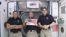 Die US-Raumfahrer Robert Behnken (l) und Chris Cassidy (r) sowie Commander Douglas Hurley (M) halten eine US-Nationalflagge in die Höhe, die vor fast einem Jahrzehnt auf der Internationalen Raumstation zurückgelassen wurde. | Bild: dpa-Bildfunk/Uncredited