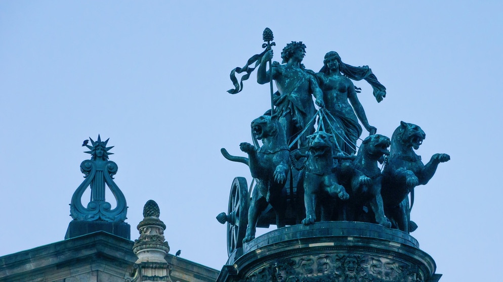 Ariadne und Dionysos lenken den Streitwagen auf dem Dach der Semperoper in Dresden. Der griechischen Mythologie nach warf Dionysos, Gott des Weines, das Krönchen der Königstochter von Kreta an den Himmel, wo es als Sternbild Nördliche Krone verewigt ist. | Bild: picture-alliance/Zoonar | Ullrich Gnoth