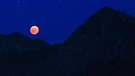 Blutmond während der totalen Mondfinsternis am 27. Juli 2018 zwischen dem Nebelhorn und dem Rubihorn, darunter sieht man die beleuchtete Schöllanger Burgkirche und die Geißalpe, aufgenommen von Roswitha Schöllhorn. | Bild: Roswitha Schöllhorn