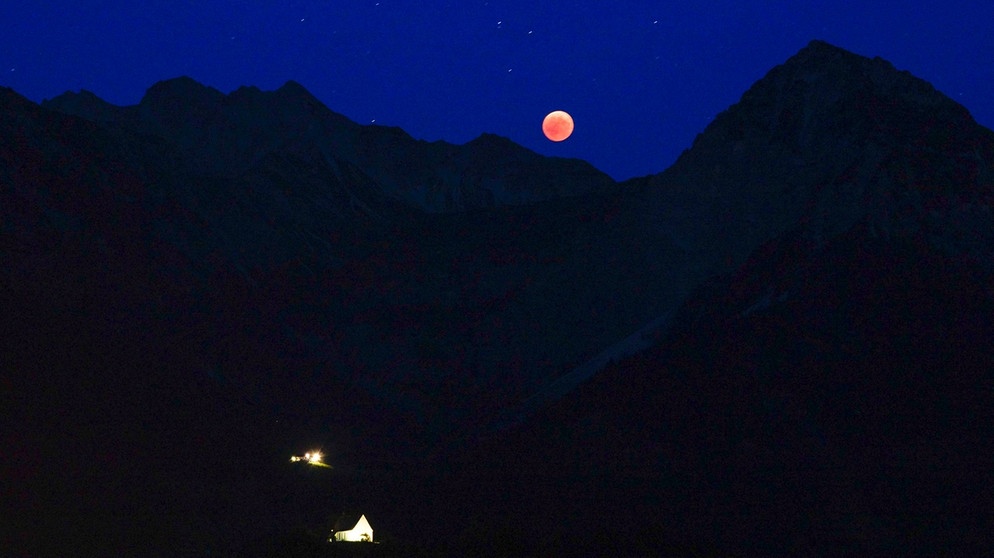 Blutmond während der totalen Mondfinsternis am 27. Juli 2018 zwischen dem Nebelhorn und dem Rubihorn, darunter sieht man die beleuchtete Schöllanger Burgkirche und die Geißalpe, aufgenommen von Roswitha Schöllhorn. | Bild: Roswitha Schöllhorn